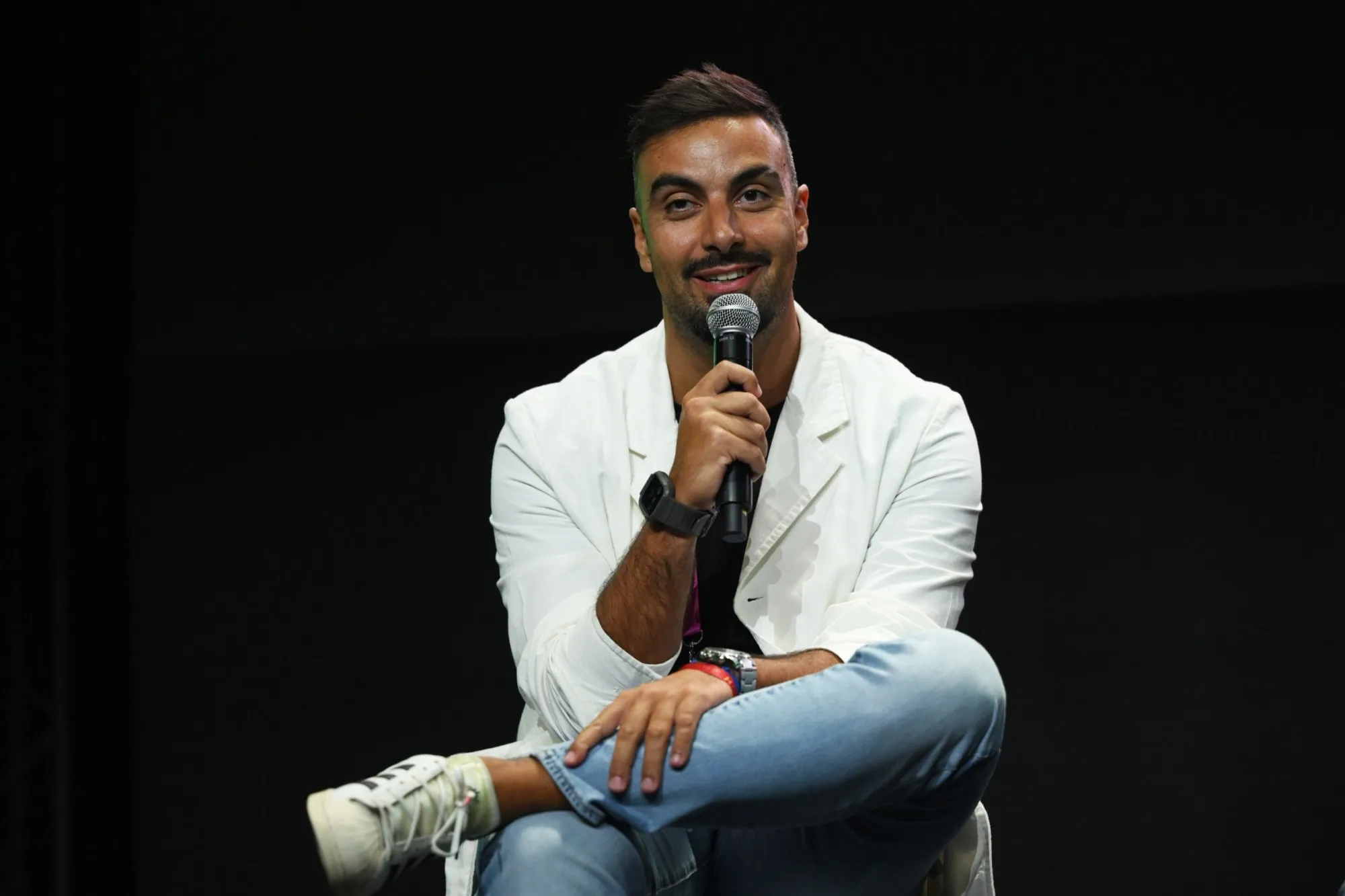 David Olim seated on a stool with a microphone, answering an interview