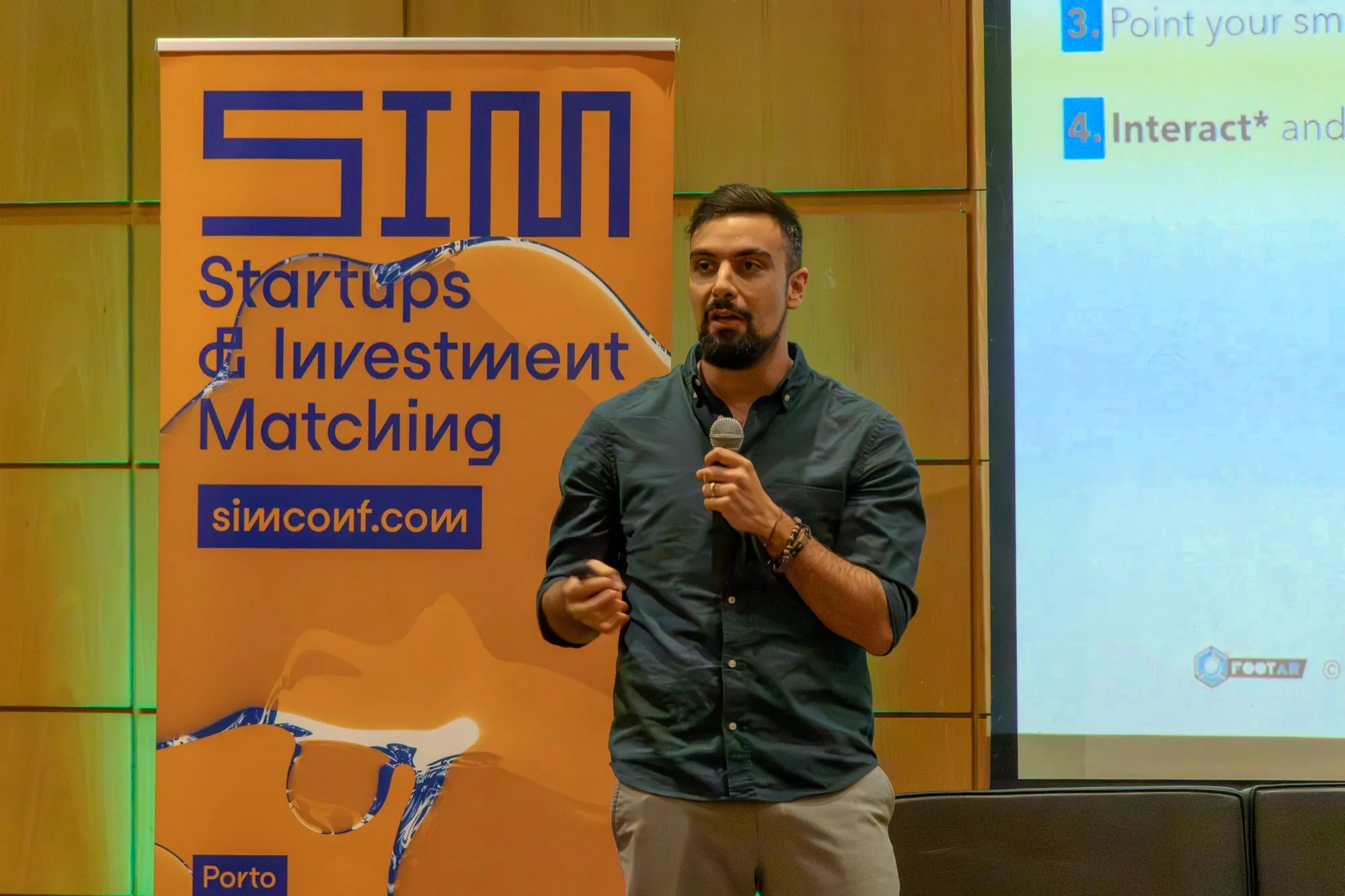 David Olim speaking with a microphone in front of the SIM conference banner
